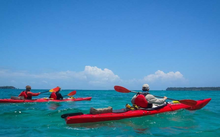 Two red kayaks are paddled by outward bound students on very blue water, with a blue sky above.